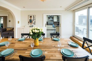 Un comedor con una mesa de madera preparada para cuatro, platos color turquesa y un jarrón con flores blancas.