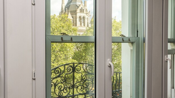 A view through a window with a wrought iron balcony and a building with a pointed roof and towers in the background.