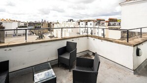 A rooftop terrace with wicker furniture and a view of the cityscape.