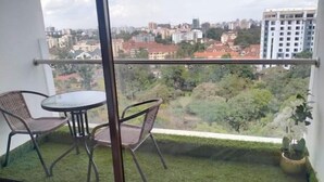 Un balcon avec une porte vitrée, deux fauteuils en osier, une petite table ronde et un pot de fleurs.