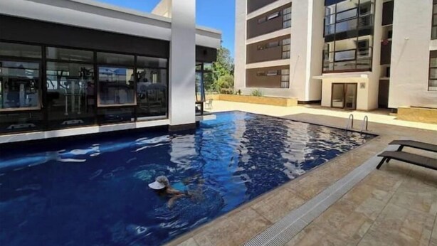 Une piscine où une personne nage, entourée d’immeubles modernes dotés de grandes fenêtres.