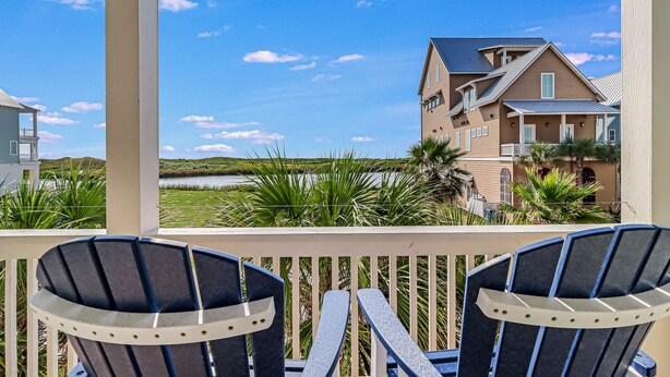 A balcony with two Adirondack chairs overlooking a residential area with houses and a body of water. - Luxe Palmilla Beach home with Gulf view, guest suite, pool access, walk to beach (Port Aransas)