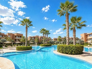 A resort pool with palm trees and lounge chairs, surrounded by buildings.