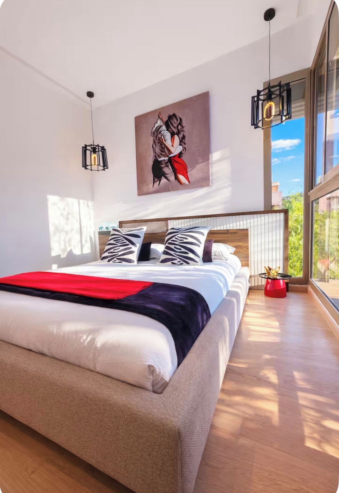Une chambre à coucher moderne avec un grand lit, un tableau au mur et une vue sur l’extérieur.