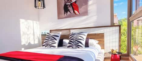 Un dormitorio moderno con una cama grande, un cuadro en la pared y vistas al exterior.
