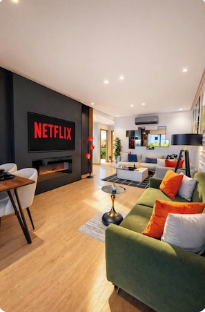 A modern living room with a flat-screen TV, a fireplace, a sofa, and a dining area.
