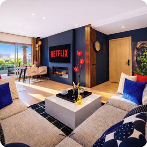 A modern living room with a flat-screen TV, a fireplace, and a dining area with chairs and a table.