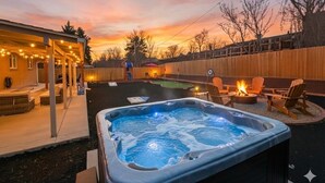 A backyard with a hot tub, outdoor seating, and a wooden fence. - Denver Ultimate Group Getaway: Mini-Golf, Hot Tub, Fire Pit, Games & Playground (Denver)