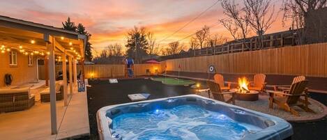 A backyard with a hot tub, outdoor seating, and a wooden fence.