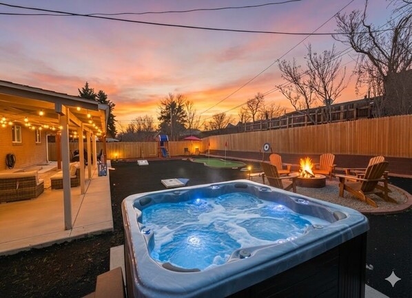 Un patio trasero con jacuzzi, mobiliario exterior y una cerca de madera.