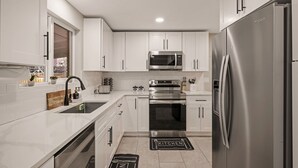 A modern kitchen with white cabinets, stainless steel appliances, and a black kitchen mat. - Denver Ultimate Group Getaway: Mini-Golf, Hot Tub, Fire Pit, Games & Playground (Denver)