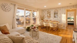 A cozy living room with a sofa, a dining area with a table and chairs, and a large window with a view of the outside. - Denver Ultimate Group Getaway: Mini-Golf, Hot Tub, Fire Pit, Games & Playground (Denver)