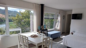 Una stanza con un tavolo da pranzo, sedie, un divano, un letto e ampie finestre vista su spazi verdi e colline.