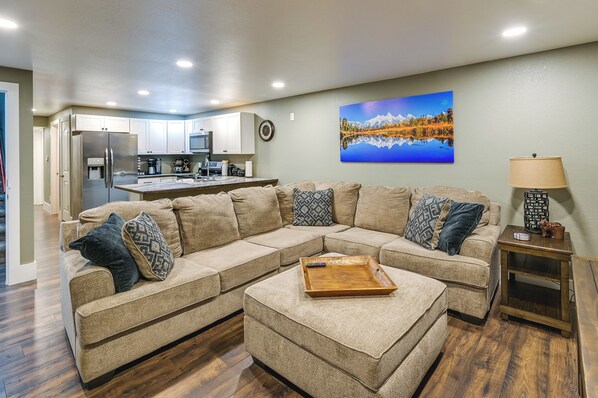 A living room with a sectional sofa, a wooden coffee table, and a kitchen in the background. - Laramie Gem < 1/2 Mi to University of Wyoming! (Laramie)