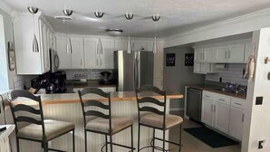 Una cocina moderna con armarios blancos, un refrigerador de acero inoxidable y una zona de bar con taburetes.