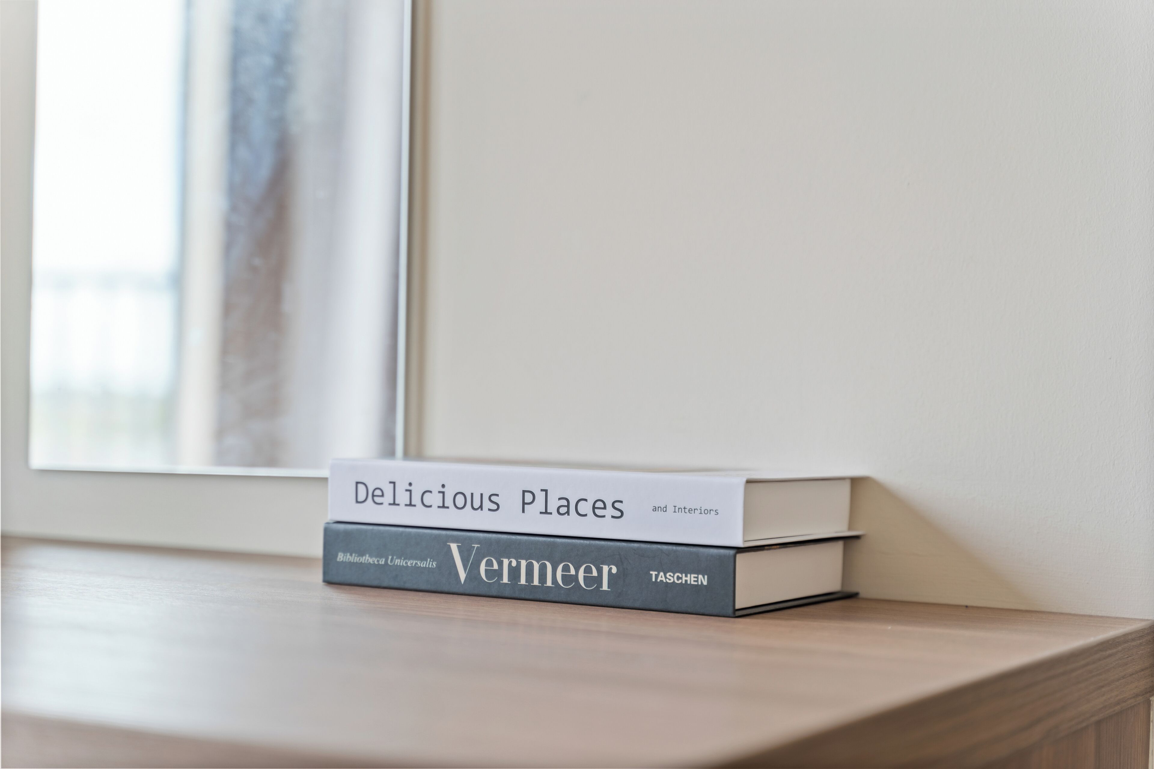 Un libro titulado 'Delicious Places and Interiors' de Vermeer sobre una superficie de madera cerca de una ventana.