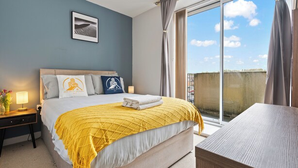 A neatly made bed with a yellow throw blanket, a bedside lamp, and a framed picture on the wall. - 2-BR serviced Apartment In Telford - W/Wi-fi /Netflix (Telford)