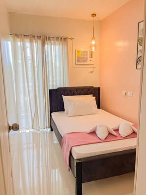 Un dormitorio con cama, mesita de noche, ventana con cortinas, aire acondicionado instalado en la pared y lámpara.