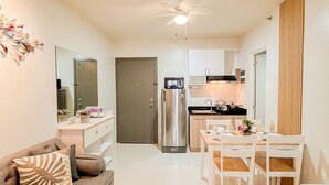 Una cocina moderna con armarios blancos, un refrigerador de acero inoxidable y un microondas. Hay una mesa de comedor con sillas y un ventilador de techo.