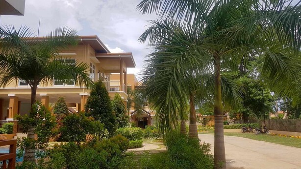 Un hotel con varios pisos, un área de piscina y abundante vegetación, incluyendo palmeras.