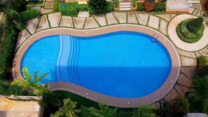 Vista aérea de una piscina rodeada de terrazas de madera y zonas ajardinadas.