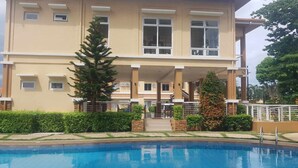 Un hotel de varios pisos con piscina, una escalera que conduce a la entrada y un jardín bien cuidado.