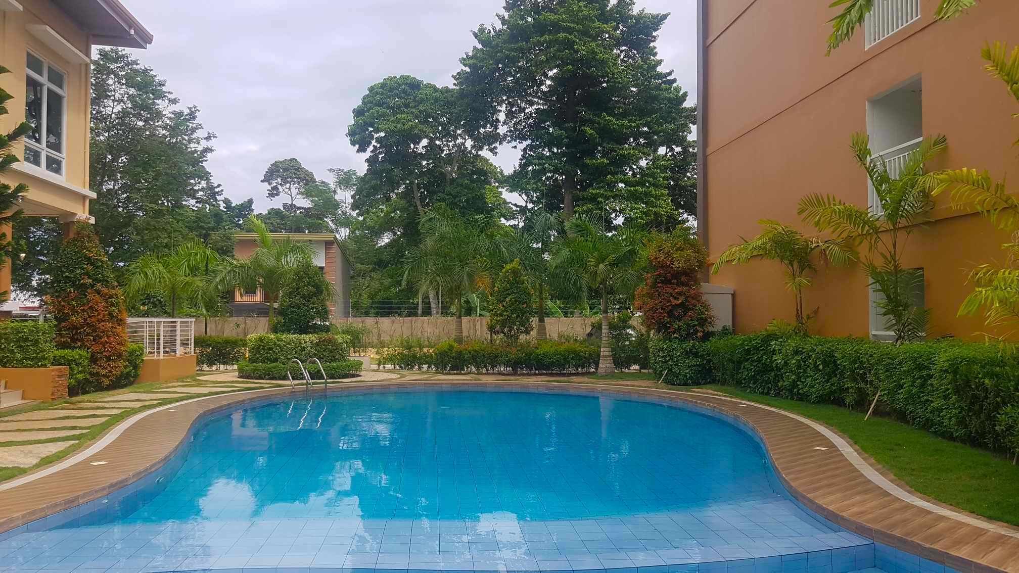 Una piscina con bordo curvo, circondata da un giardino curato e da un edificio con facciata color crema.