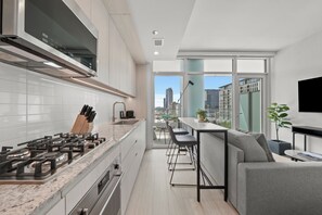 A modern kitchen with a gas stove, white cabinets, and a view of the city through large windows. - Level Fulton Market - Open Concept studio with full kitchen and luxury bathroom (Chicago)