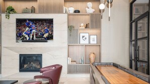 A modern living room with a fireplace, a flat-screen TV, a shuffleboard table, and leather chairs. - Level Fulton Market - Open Concept studio with full kitchen and luxury bathroom (Chicago)