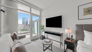 A modern hotel room with a large window, a flat-screen TV, a desk, a bedside table with a lamp, and a bed. - Level Fulton Market - Open Concept studio with full kitchen and luxury bathroom (Chicago)