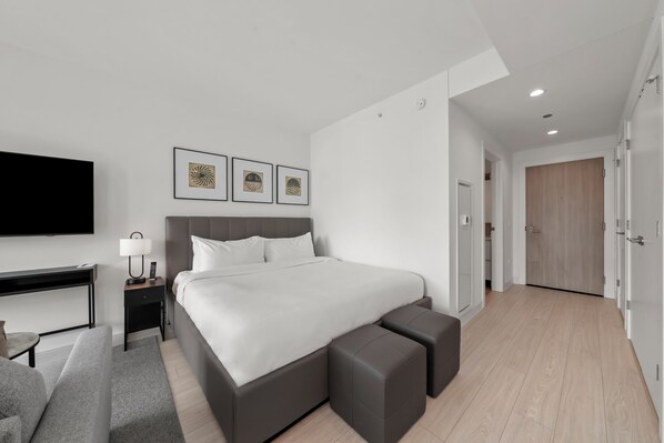 A modern hotel room with a large bed, a desk with a lamp, a flat-screen TV, and artwork on the wall.