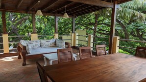 Una terraza de madera con un sofá, sillas, una mesa y lámparas colgantes.