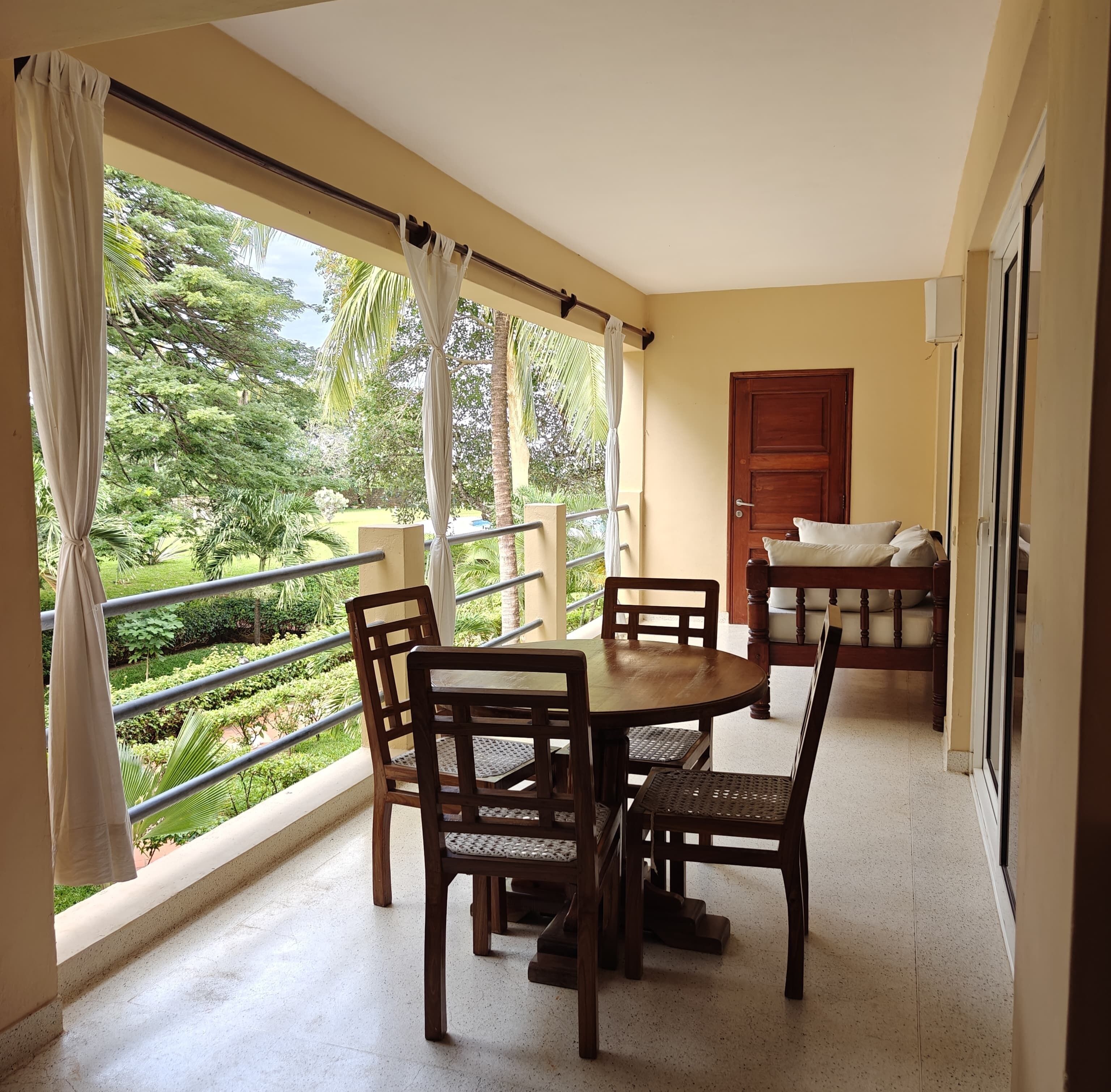 Un balcon avec une table et des chaises en bois, une porte et une vue sur un jardin.