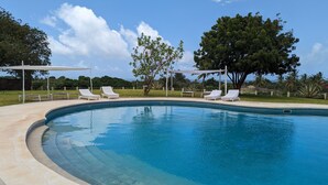 Una piscina con sillas reclinables blancas y un árbol al fondo.