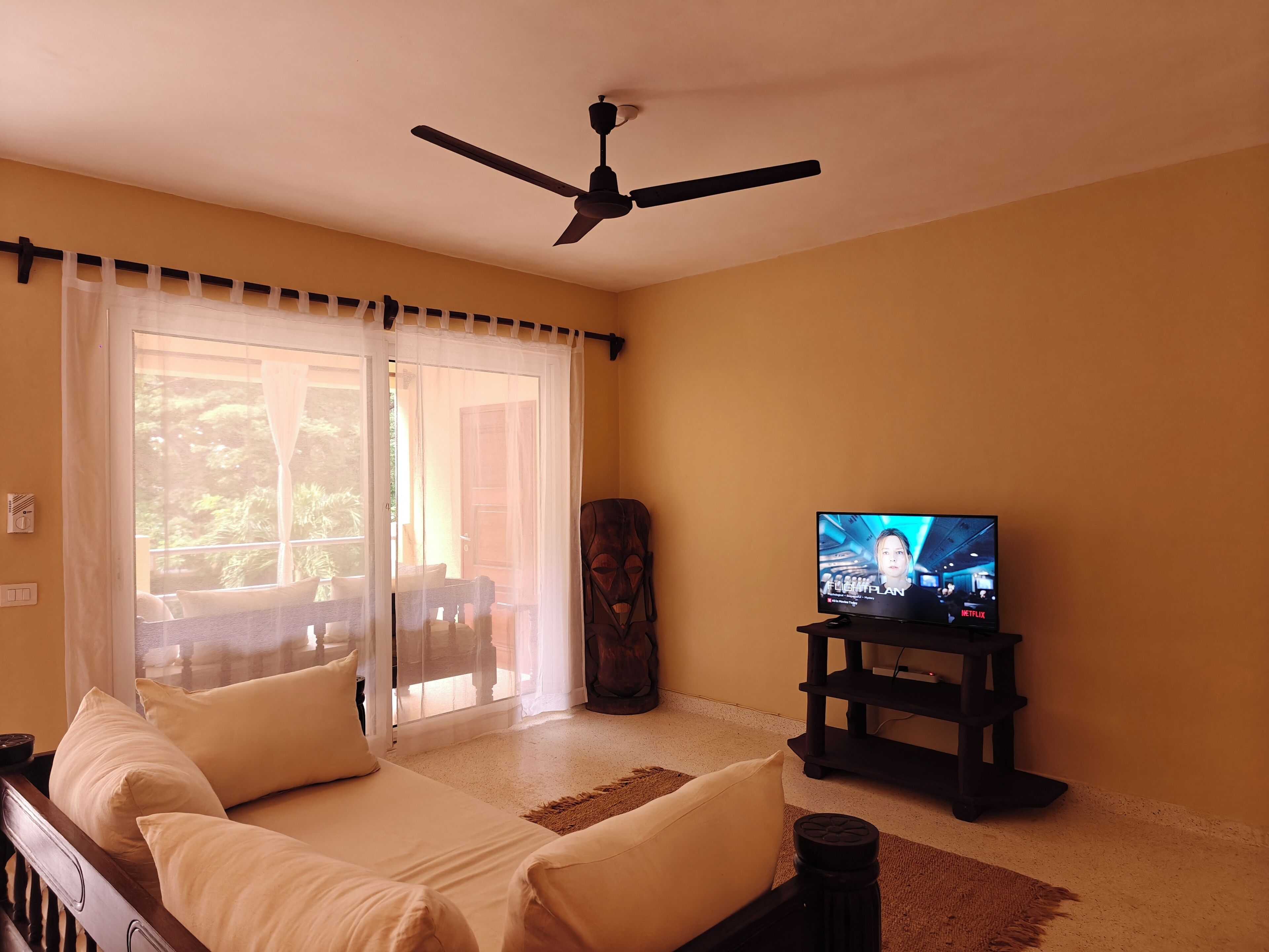 Una sala de estar con un sofá, una televisión, un ventilador de techo y vistas a través de una puerta de cristal.
