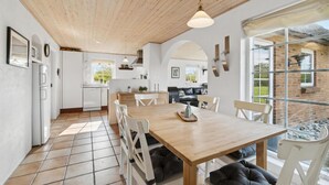 Uma cozinha espaçosa com armários brancos, uma mesa de jantar de madeira e uma janela grande com vista para o jardim.