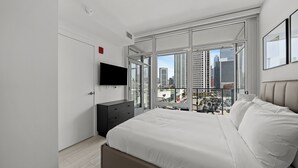 A modern bedroom with a large bed, a flat-screen TV mounted on the wall, and a city view through floor-to-ceiling windows. - Level - Fulton market Modern two bedroom two bath with full kitchen and balcony (Chicago)