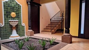 A courtyard with a tiled floor, a small garden area with plants, a white pedestal, and a staircase leading to an upper level. - Luxurious colonial style home! (San Pedro Las Huertas)