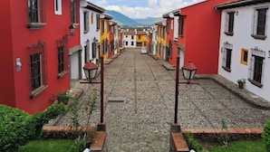 A cobblestone street lined with colorful buildings, a clear sky, and distant mountains. - Luxurious colonial style home! (San Pedro Las Huertas)