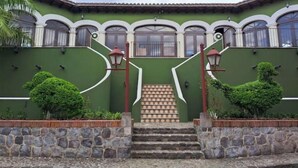 A building with a green facade, white trim, and a staircase leading to the entrance. - Luxurious colonial style home! (San Pedro Las Huertas)