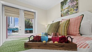 A hotel room with a bed, a wooden tray with glasses and flowers, and a painting on the wall. - Close to Everything in Gulf Shores! 5 BR house w/Private Pool (Gulf Shores)
