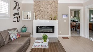 A modern living room with a fireplace, a sofa, a coffee table, and a kitchen in the background. - CentralDowntownSanJose-Stunning, fireplace Modern Craftsman house/SAP, Airport (San Jose)
