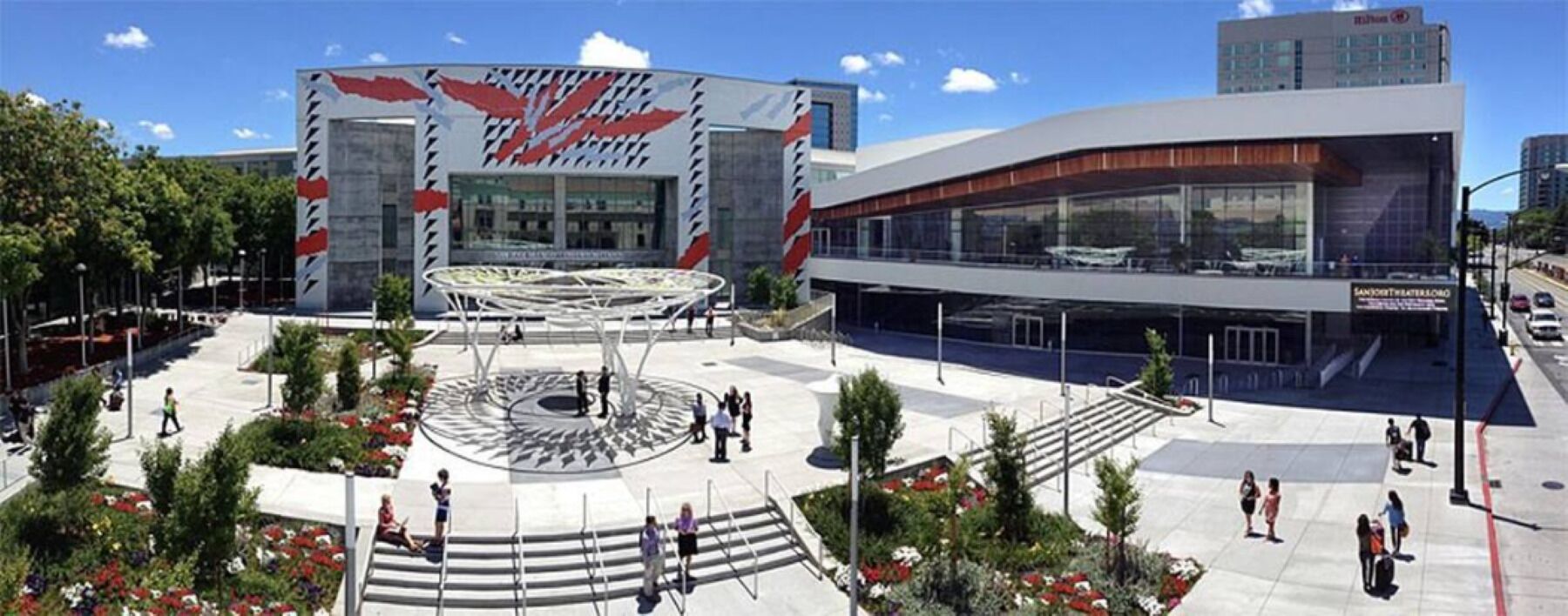 A modern hotel with a circular plaza, outdoor seating, and a large glass facade.