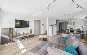 Un salon moderne avec un canapé gris, un plancher en bois et un coin repas comprenant une table et des chaises.