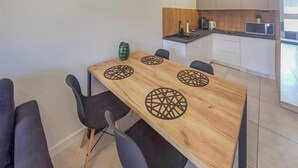 Un coin repas avec une table en bois et quatre chaises, une cuisine en arrière-plan et une vue sur l’extérieur.