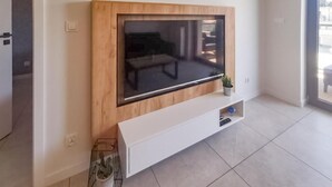 Un salon moderne avec un grand téléviseur à écran plat fixé sur un meuble mural en bois, une petite plante en pot et un sol carrelé.