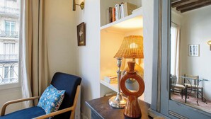 A room with a blue chair, a bookshelf, a lamp, and a view of the outside. - Central Duplex Notre Dame (Paris)