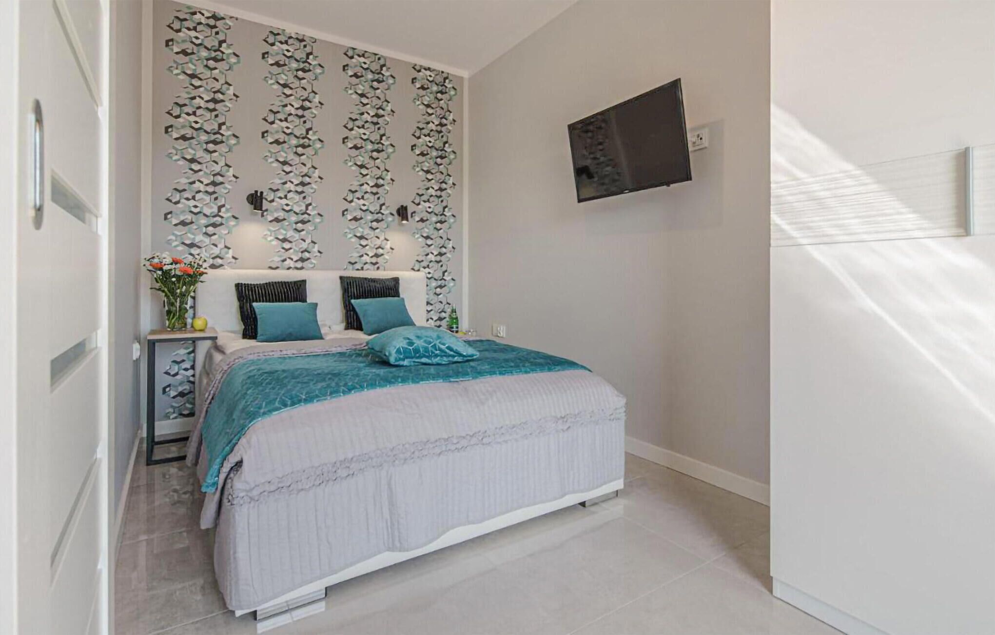 Une chambre à coucher comprenant un lit, une table de chevet, un téléviseur et un mur orné d’un motif géométrique.