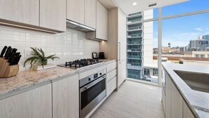 A modern kitchen with stainless steel appliances, a marble countertop, and a city view through large windows. - Level - Fulton Market spacious 2 bedroom, 2 bath suite with full kitchen (Chicago)