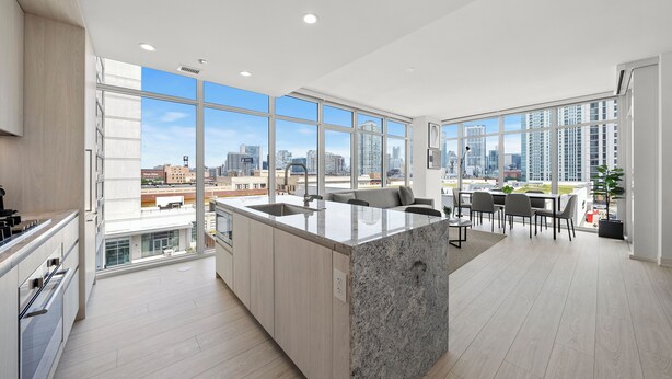 A modern kitchen with a large island, a dining area with a view of the city, and a spacious living area with a large window. - Level - Fulton Market spacious 2 bedroom, 2 bath suite with full kitchen (Chicago)